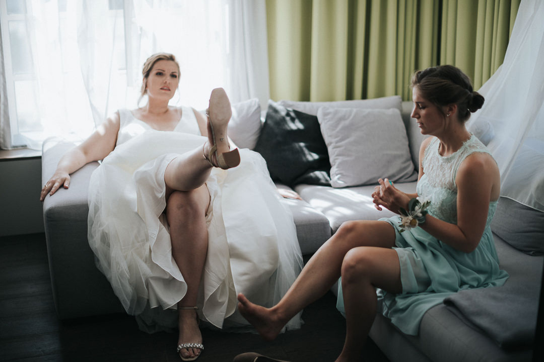 Braut sitzt mit ihrer Trauzeugin auf der Couch und begutachtet ihrer Schuhe.