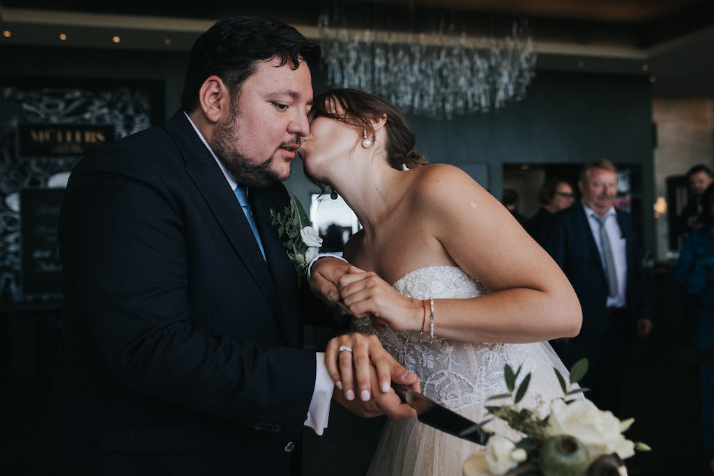 Braut gibt dem Bräutigam einen Kuss beim Tortenanschnitt.